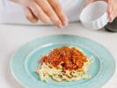 Cooking Class - Italian Pasta al Fresco in Downtown Dallas: Seasoning tomato pasta dish – A plate of pasta topped with tomato sauce being finished with a sprinkle of seasoning from a small white bowl.