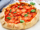 Cooking Class - Flavors of Paris – Date Night in South Bay & Peninsula: Rustic tomato tart with basil – A golden galette-style tart filled with cherry tomatoes and topped with fresh basil leaves on a white surface.