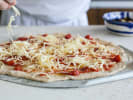 Cooking Class - Rustic Pizza Perfection: topping a homemade pizza with cheese