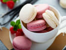 Cooking Class - Macaron Dreams in Manhattan: Vanilla and raspberry macarons in teacup â€“ A mix of white and pink macarons stacked in a teacup with fresh raspberries and mint on the side.