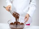 Cooking Class - Flavors of Paris – Date Night in South Bay & Peninsula: Whisking melted chocolate in glass bowl – A person in a white chef’s coat whisking glossy melted chocolate in a clear glass bowl.