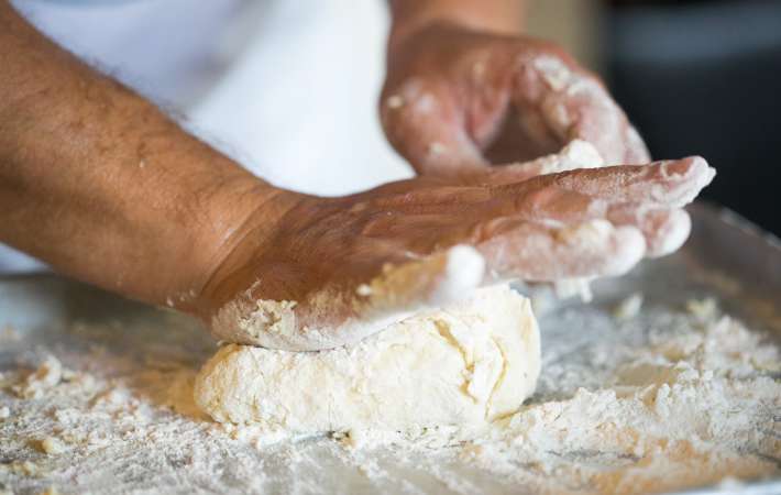 chef kneading deep dish pizza dough on a floured work surface