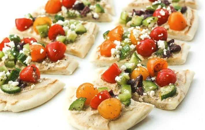 greek salad hummus flatbread is topped with fresh vegetable and savory feta cheese