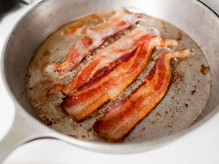 bacon strips frying in a metal skillet Shot