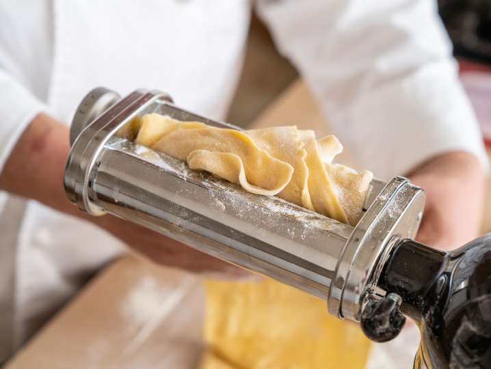 chef rolling fresh pasta dough through a pasta roller attachment Shot