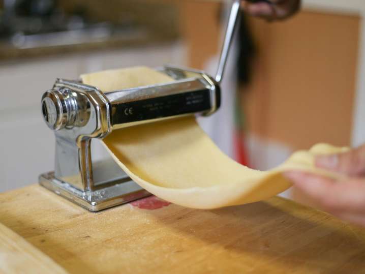 chef's hand rolling sheet of fresh pasta dough through a pasta roller Shot