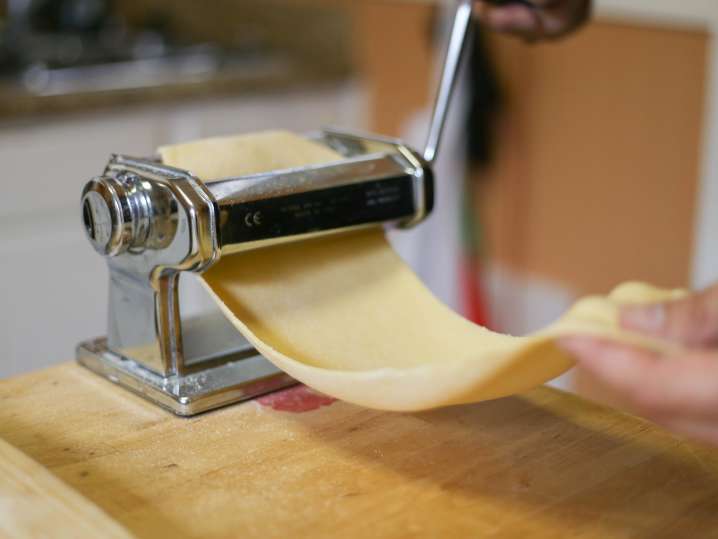 chef's hand rolling sheet of fresh pasta dough through a pasta roller Shot