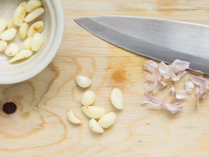 peeled cloves of garlic and a knife on a cutting board Shot