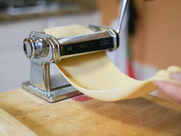 chef's hand rolling sheet of pasta dough through pasta roller Shot