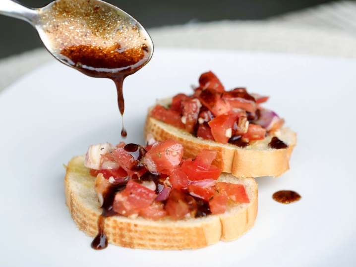 spooning balsamic vinegar over bruschetta Shot