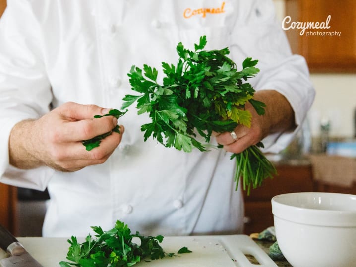 chef in Cozymeal apron is holding a batch of fresh herbs