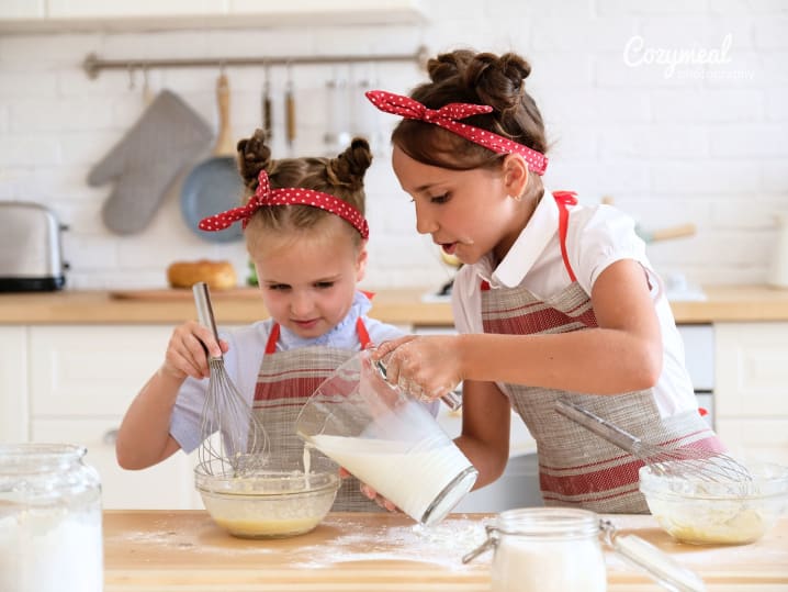 two young girls helping each other mixing baking batter in the kitchen