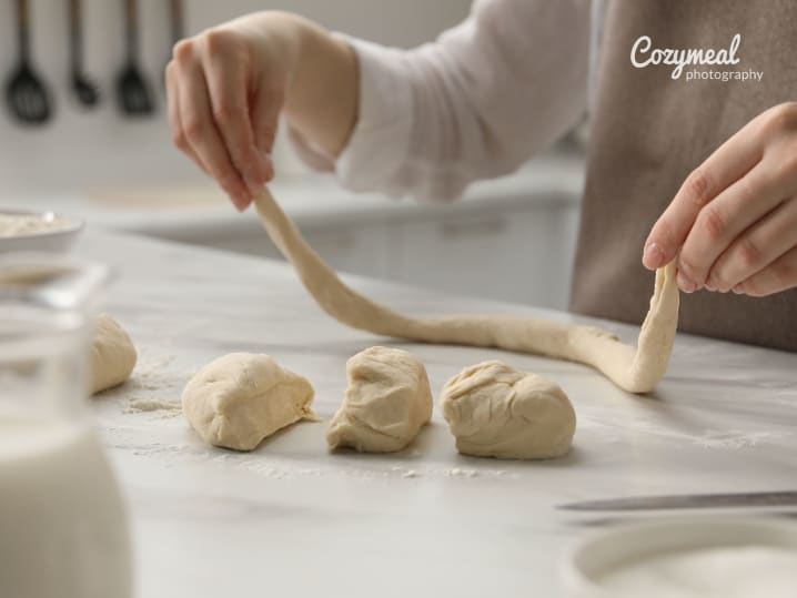 Hands rolling out soft pretzel dough into ropes with several dough portions lined up.