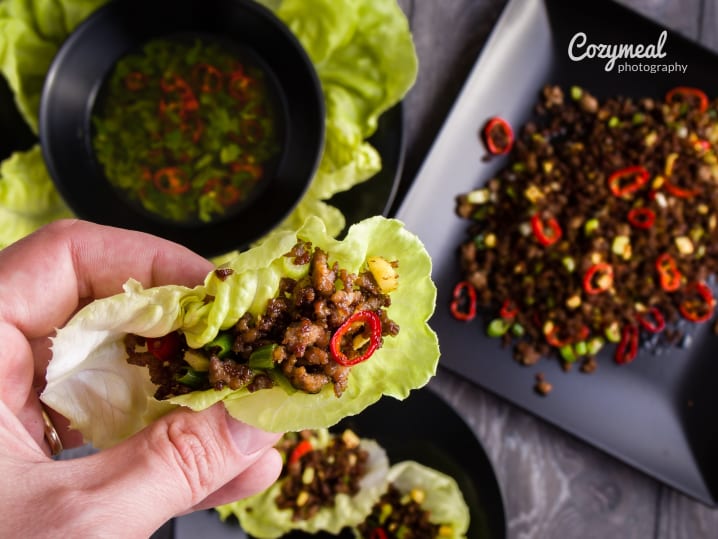 Hand assembling a lettuce wrap with beef and dipping sauce in the background.