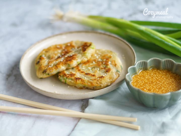 Street food-style corn and lime fritters on a plate, served with green onions and dipping sauce.
