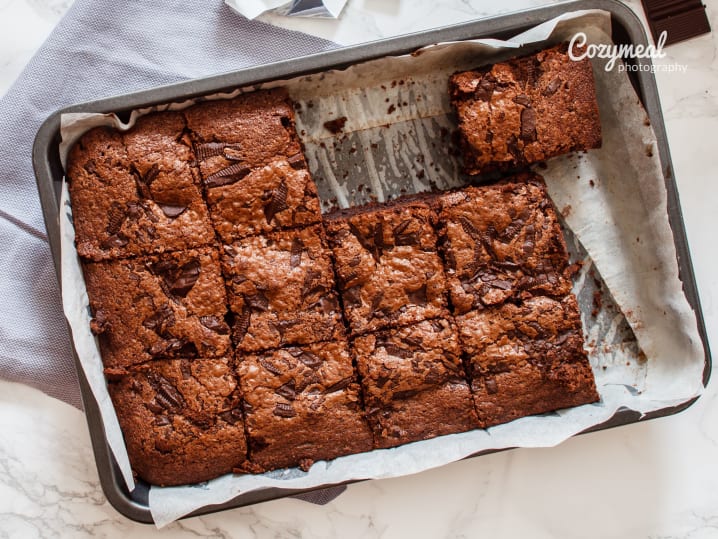 Freshly baked chocolate-cranberry brownies sliced in a parchment-lined pan.