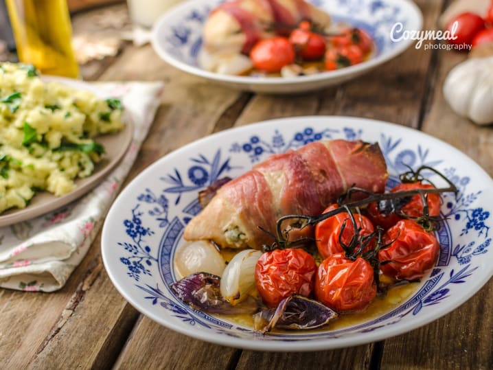 Prosciutto-wrapped chicken with chianti sauce, roasted tomatoes, and greens on a patterned plate.