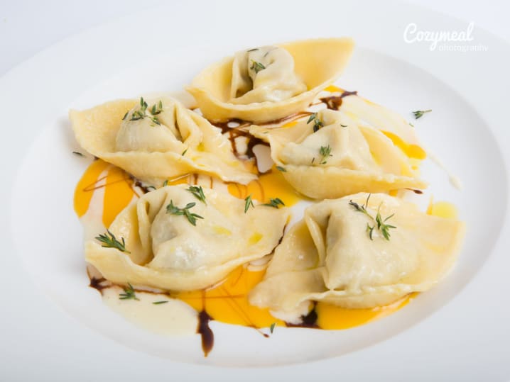 Plate of handmade pumpkin agnolotti garnished with sage and brown butter.