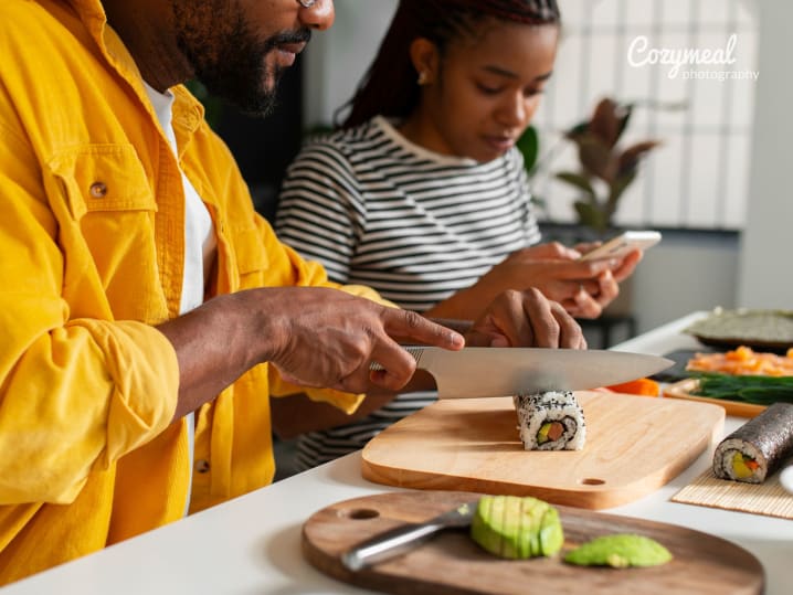 Pair making sushi together, slicing hand rolls on a cutting board.