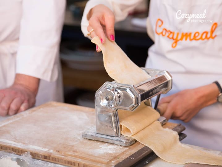 close up of two people in Cozymeal aprons making pasta sheets using pasta machine