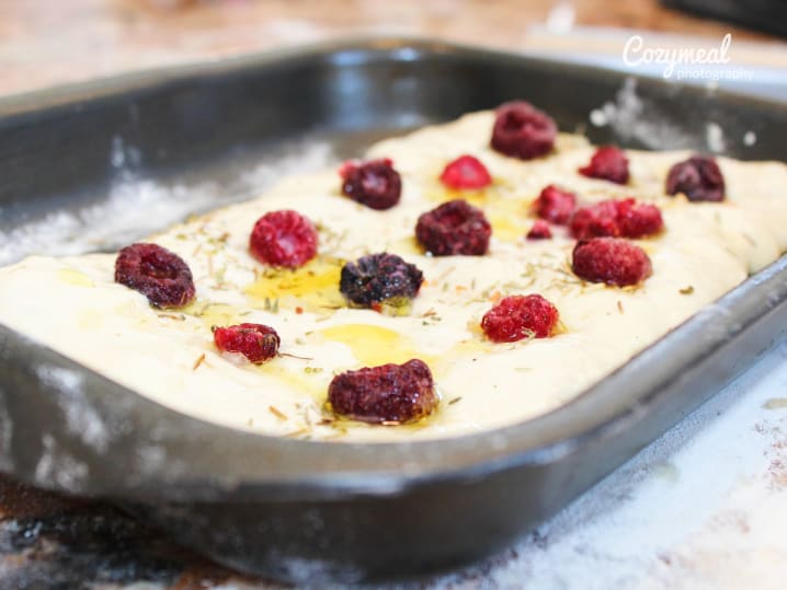 Focaccia dough topped with raspberries and dark fruit before baking.