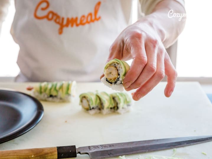 Hands slicing a sushi roll with a bamboo mat nearby on the prep surface.