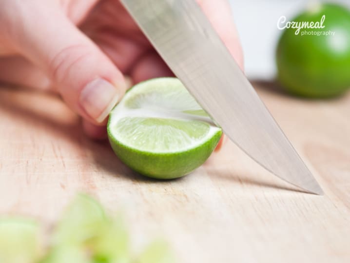 Slicing a fresh lime on a cutting board, close-up with blurred background.