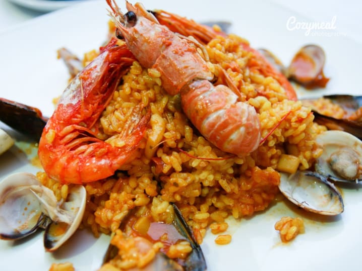 Vibrant seafood paella topped with shrimp, clams, mussels, and rice, served on a white plate.