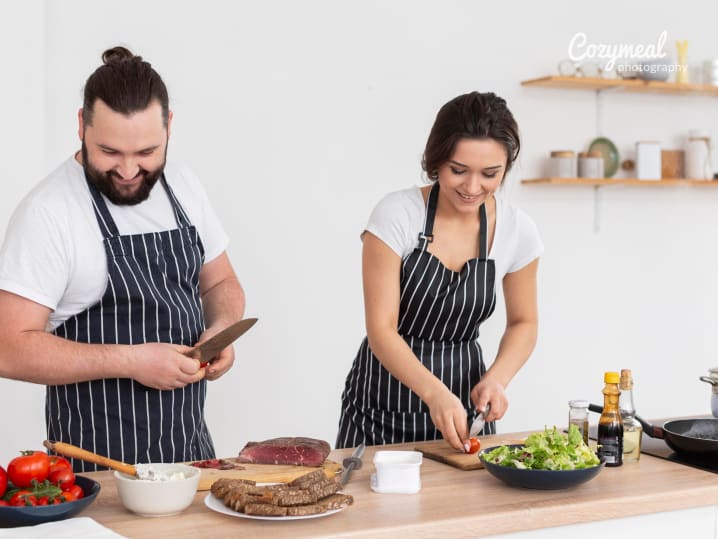 Couple preparing a meal together with wine bottles and a salad in progress.