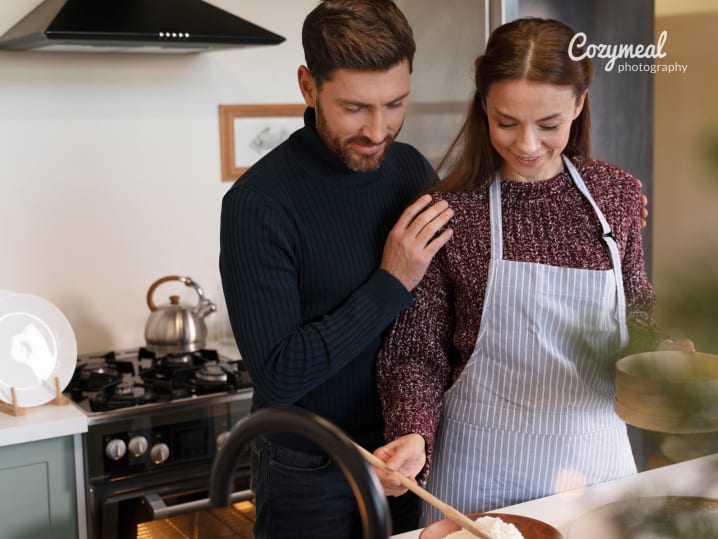 Couple cooking together at the stove, woman chopping herbs while man stands close.