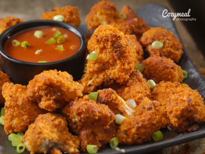 Crispy buffalo cauliflower bites garnished with scallions and served with dipping sauce.