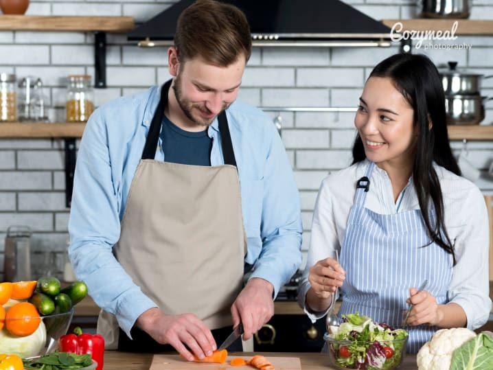 a couple cutting vegetables with aprons on in a kitchen