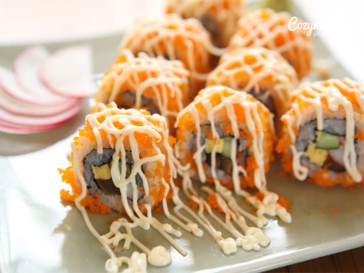 Shrimp tempura roll topped with spicy mayo and orange roe, plated on a white board.