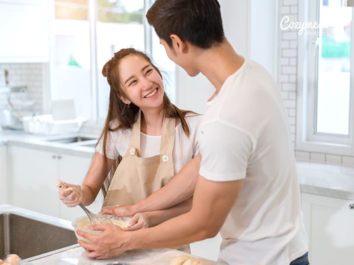 Couple preparing food together in a bright kitchen, smiling while chopping ingredients.