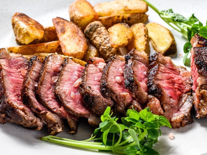 Sliced steak served with roasted potatoes and fresh herbs on a white plate.