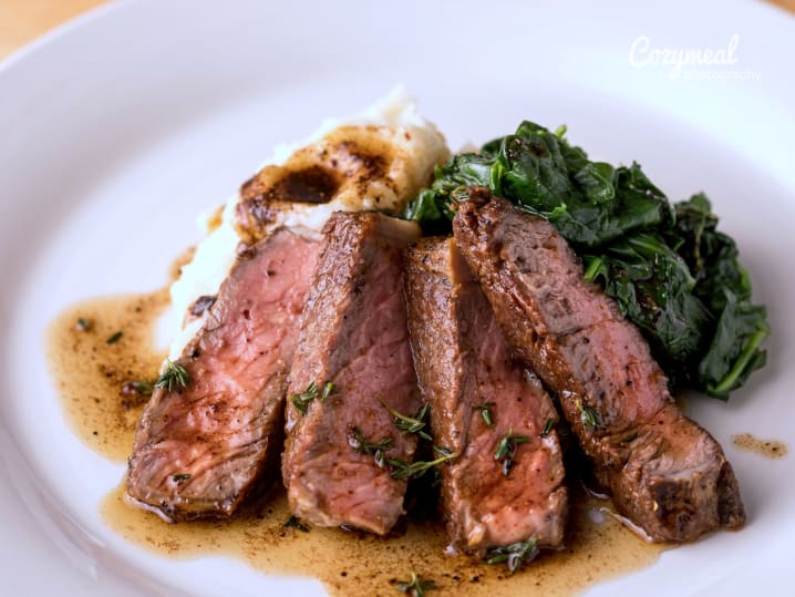 Sliced steak with gorgonzola-shallot butter, served with creamed kale on a white plate.