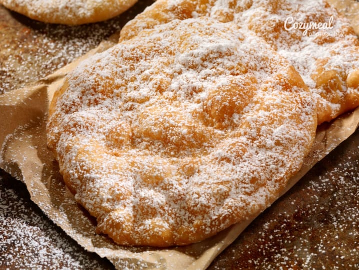 Crisp golden elephant ears dusted with powdered sugar, resting on parchment paper.