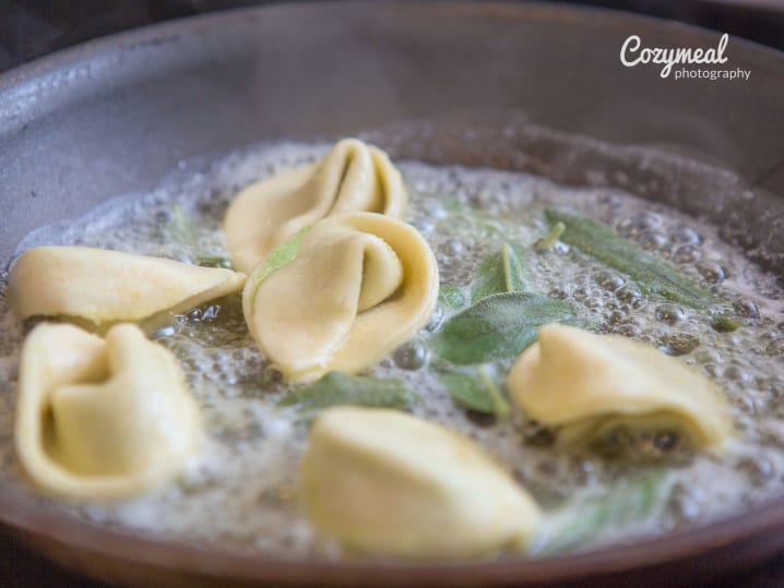 Ravioli cooking in boiling water with visible sage leaves.