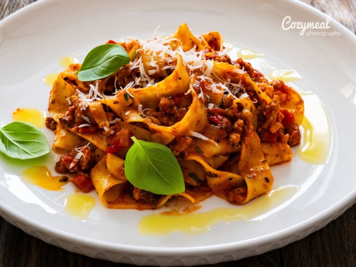 Pappardelle pasta with rich Bolognese sauce, garnished with basil.