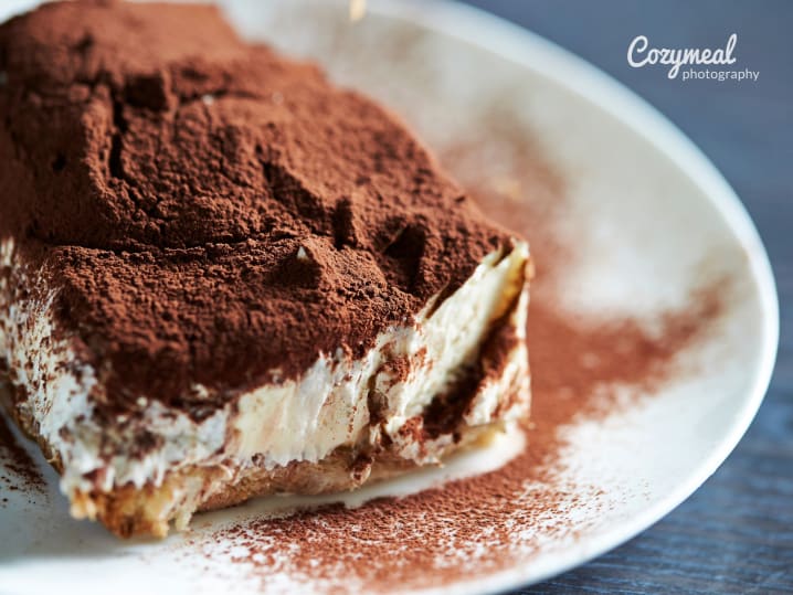 Slice of dark chocolate tiramisu dusted with cocoa powder.