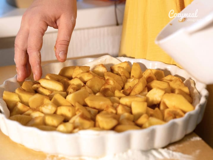 Hand arranging spiced apple slices in a tart crust before baking.