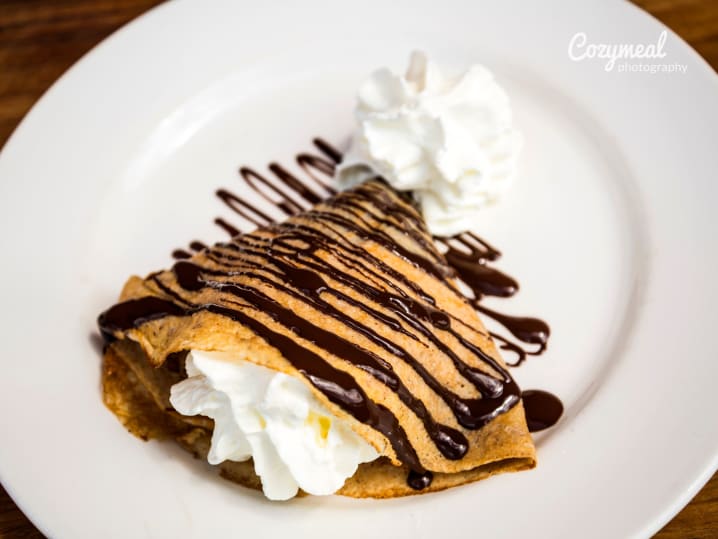 Chocolate crÃªpe topped with whipped cream and drizzled with chocolate sauce.