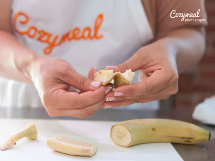 Hands slicing a peeled plantain on a cutting board, prepping for banana frita.
