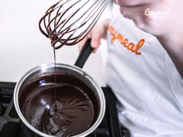 A baker pouring melted chocolate into a mixing bowl
