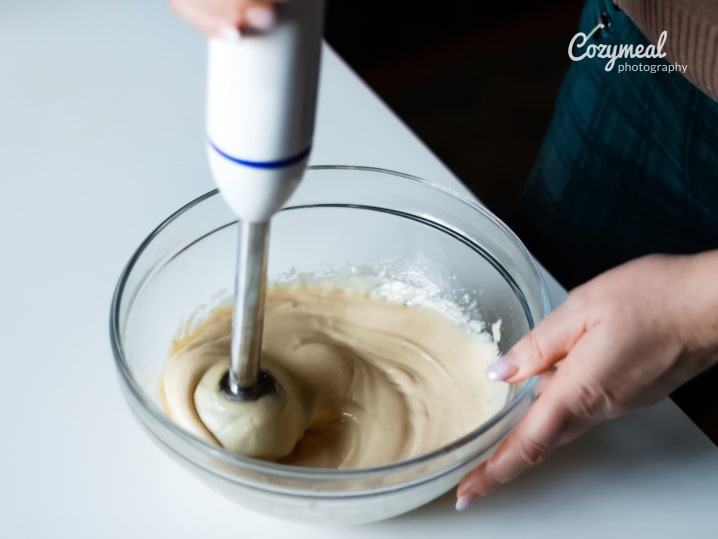 A baker whisking a creamy batter in a glass mixing bowl