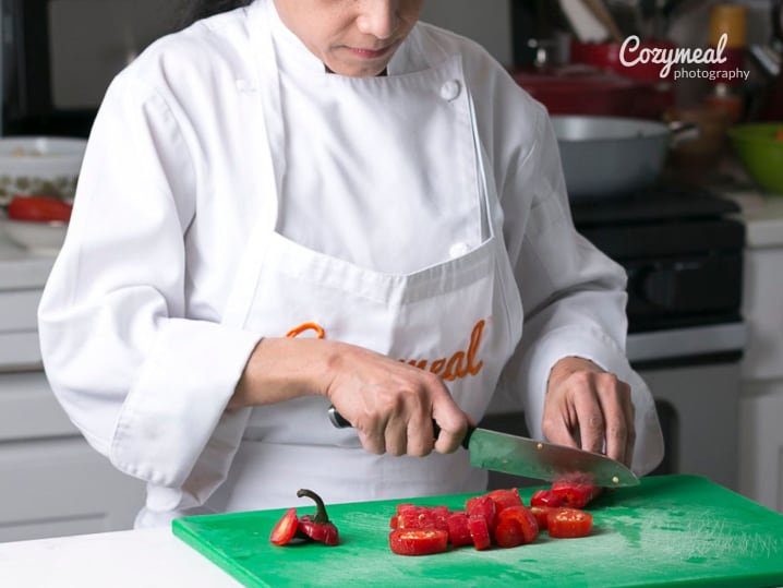 A chef chopping fresh ingredients on a green cutting board in a kitchen