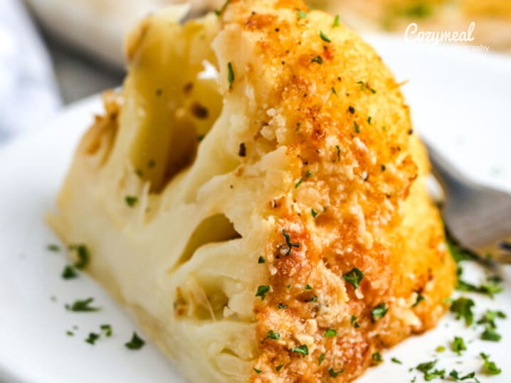 A head of cauliflower roasted to a golden brown, garnished with herbs