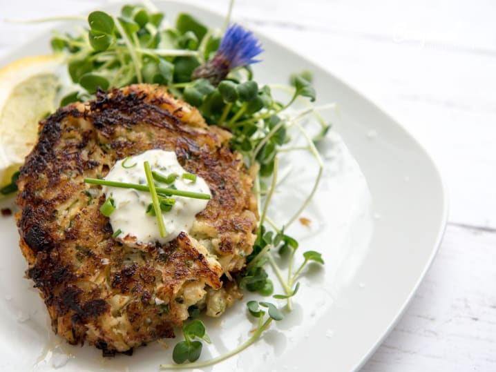 A plate of crispy golden crab cakes with greens and a lemon wedge