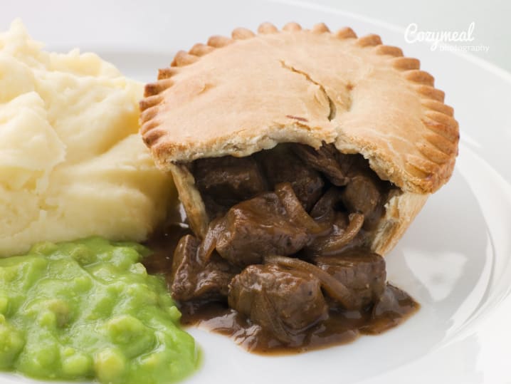 A traditional meat pie served with mashed potatoes and peas on a white plate