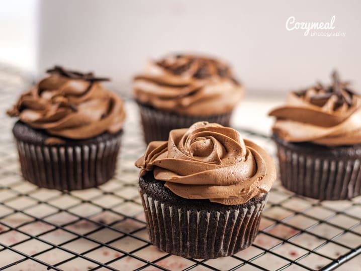 A wire rack filled with freshly baked cupcakes, cooling before decoration
